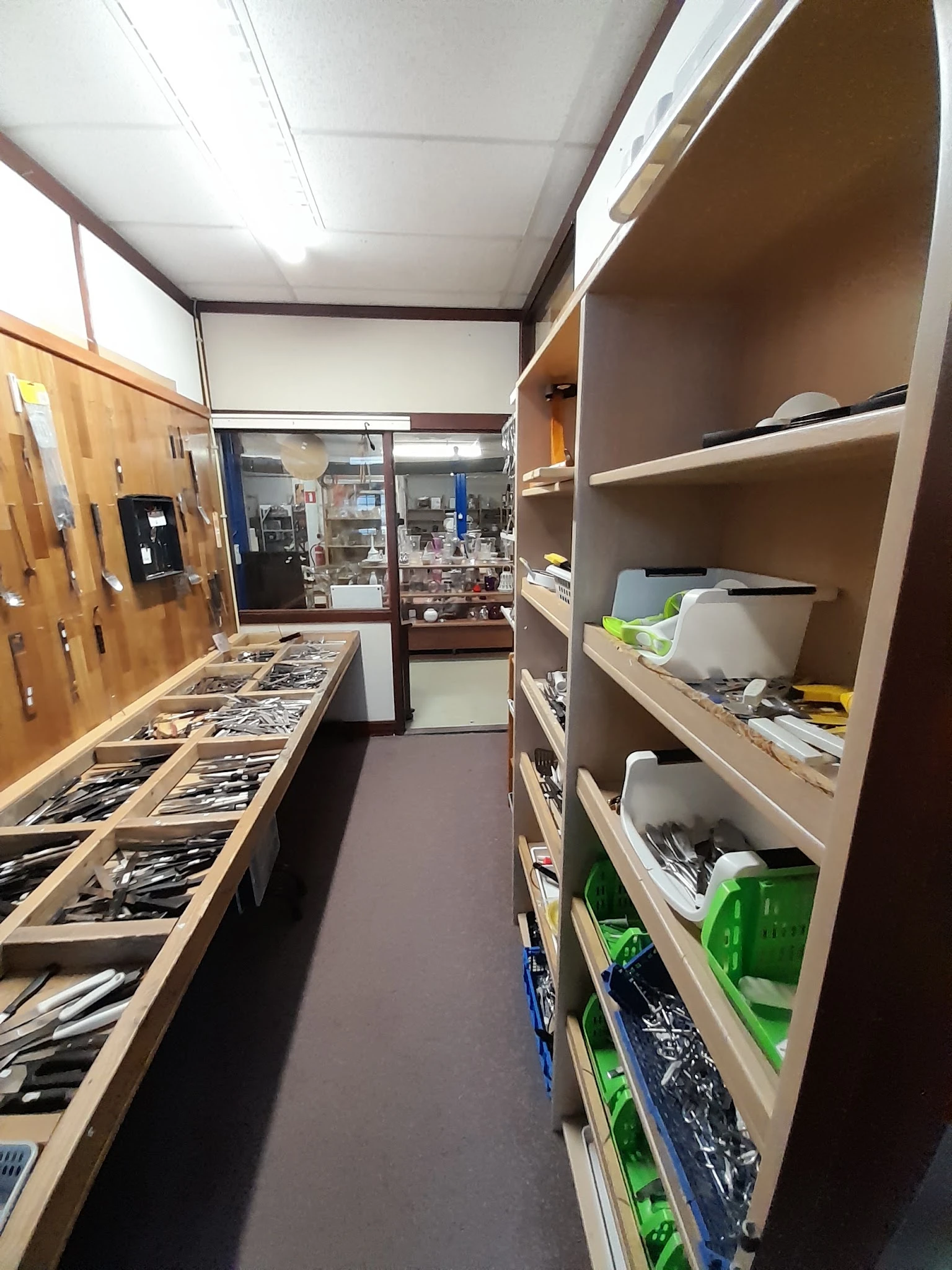 Winkelinterieur met houten stellingkasten vol met artikelen en spullen, zicht op gangpad en display aan de achterwand