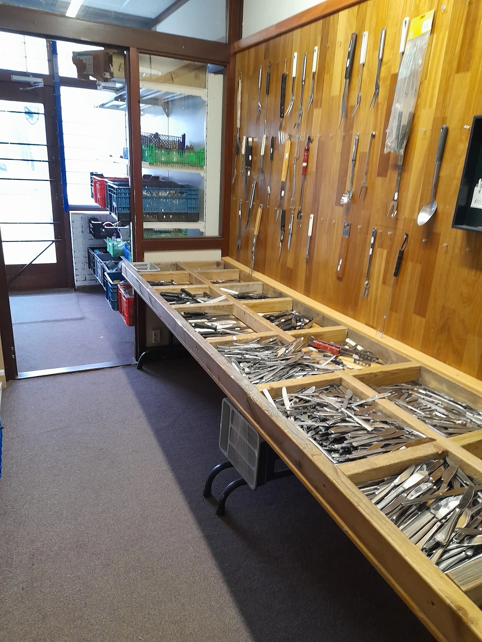 Lange houten tafel met houten bakken vol gereedschap en hardware artikelen