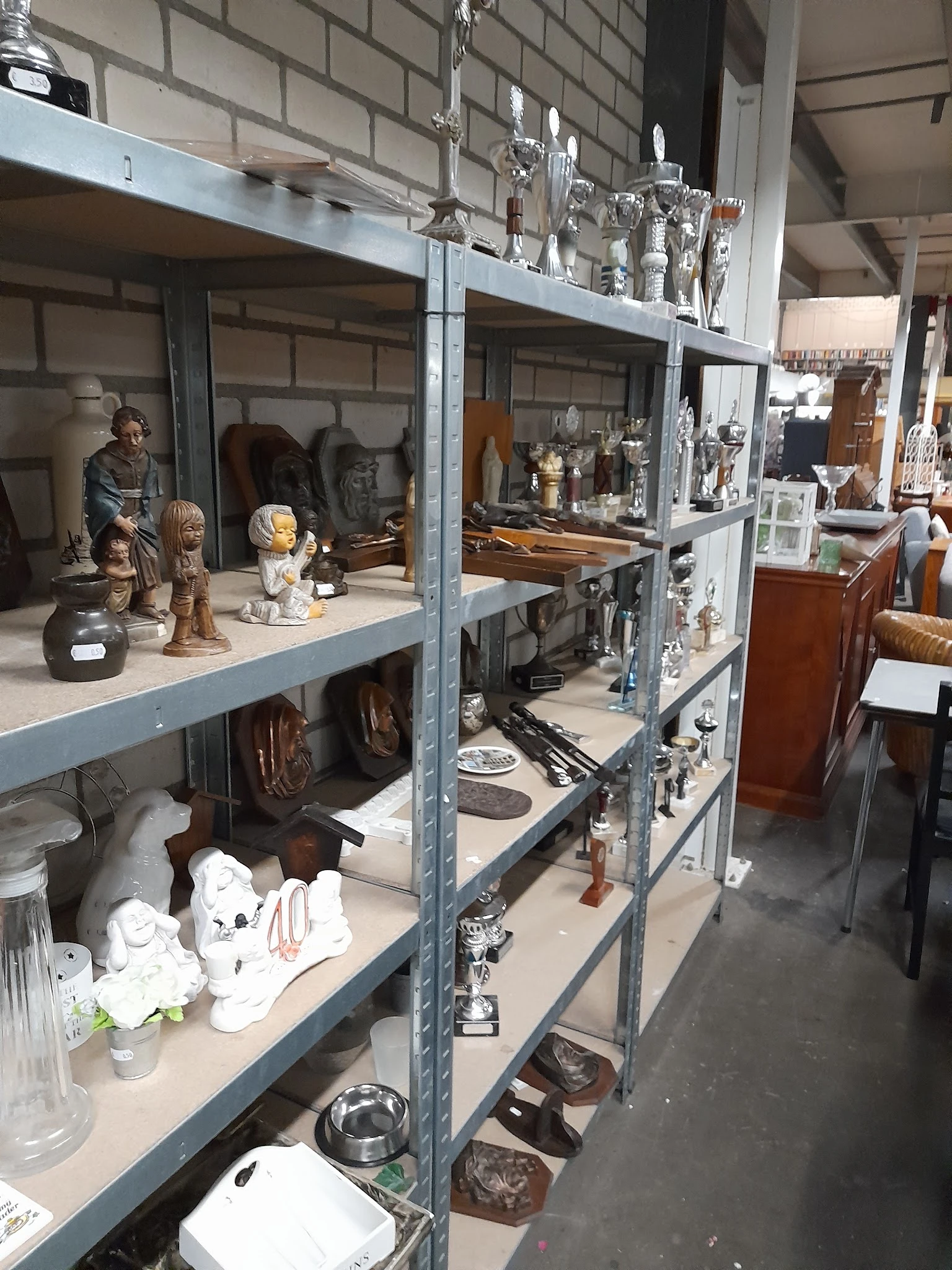 Metalen stellingen vol beeldjes, servies, decoratieve items en huishoudspullen in een kringloopwinkel