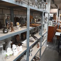 Metalen stellingen vol beeldjes, servies, decoratieve items en huishoudspullen in een kringloopwinkel
