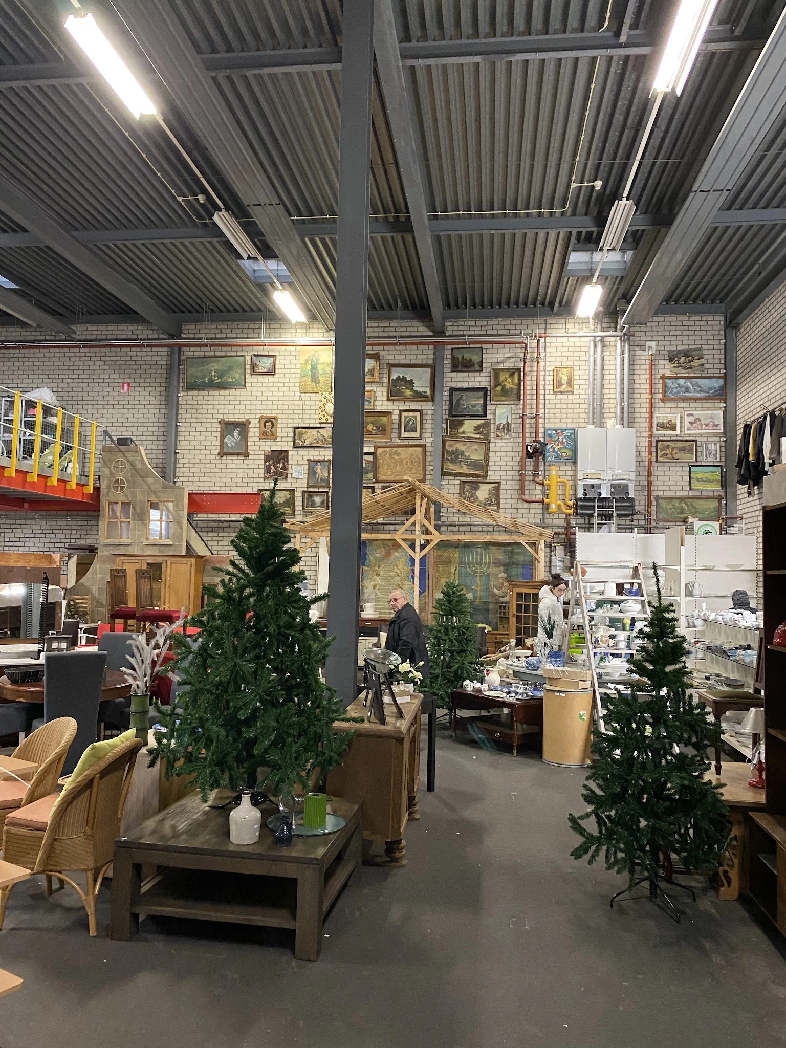 Overzicht van kringloopwinkel met diverse meubels, kunstwerk aan wanden, kunstkerstbomen en winkelartikelen