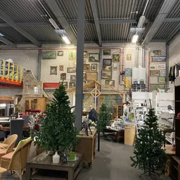 Overzicht van kringloopwinkel met diverse meubels, kunstwerk aan wanden, kunstkerstbomen en winkelartikelen