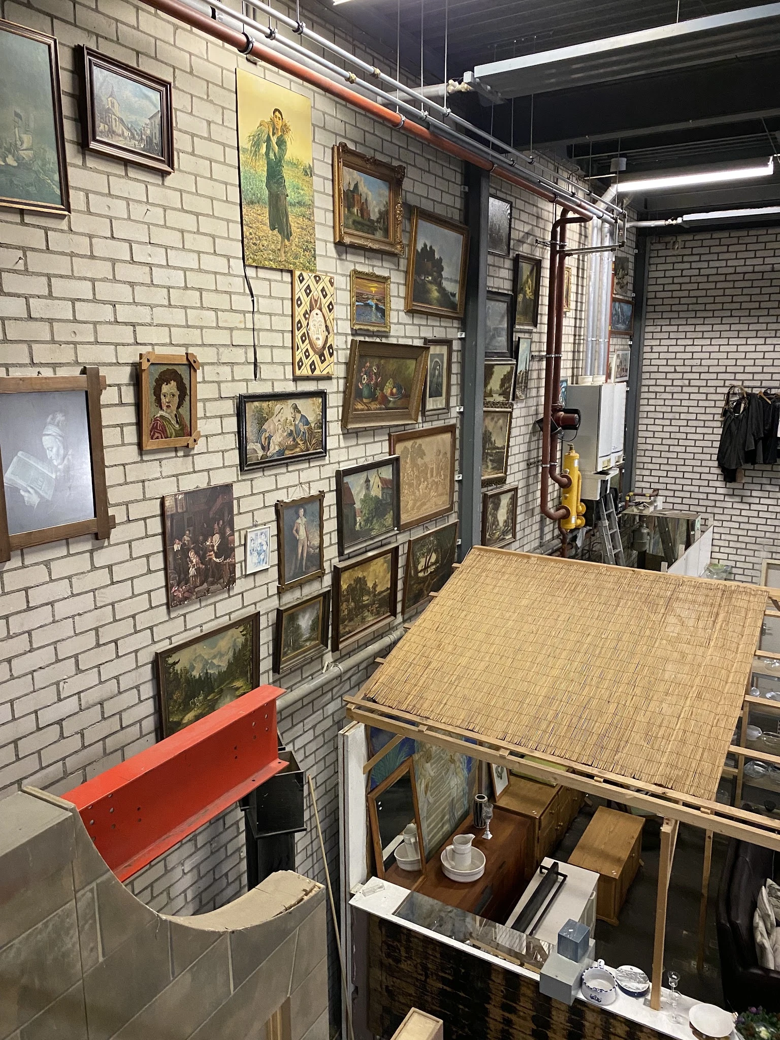 Muur met uitgestalde schilderijen en kunstwerken in houten en donkere lijsten, werktafel op voorgrond