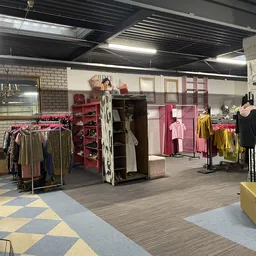 Winkelruimte met kledingrekken, rode kasten en mannequins met kleding rond podiums op gekleurde vloer