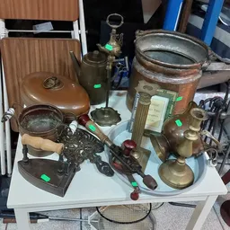 Tafel met tweedehands huishoudartikelen: koperen ketels, pannen, kandelaars en ander servies