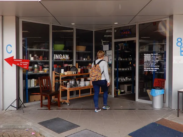 Winkelinterieur met houten tafels, stellingen met serviesgoed en huishoudartikelen, klant aan het winkelen