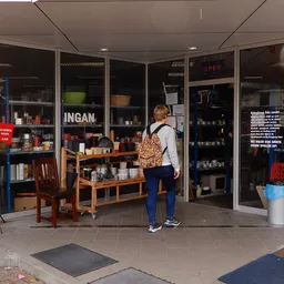 Winkelinterieur met houten tafels, stellingen met serviesgoed en huishoudartikelen, klant aan het winkelen