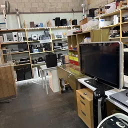 Winkelinterieur met houten stellingen vol elektronicaartikelen, een televisie en werkplekken met dozen