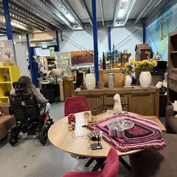Winkelinterieur met ronde tafel met roze decoratie, houten dressoir met bloemen en witte vazen, blauwe steunpilaren en gele s