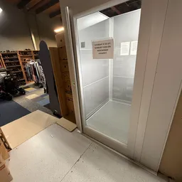 Ingang van kringloopwinkel met glazen deur, zicht op winkelruimte met stellingen en kleding op de achtergrond