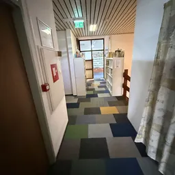 Winkelgang met gekleurde vloertegels, witte wanden en stellingen met spullen