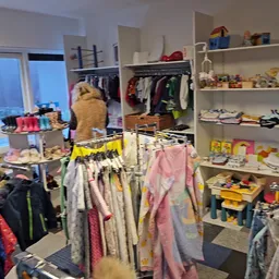 Overzicht van de winkelruimte met kledingrekken, stellingen met spullen en een geel bordje met 'BINNENKORT'