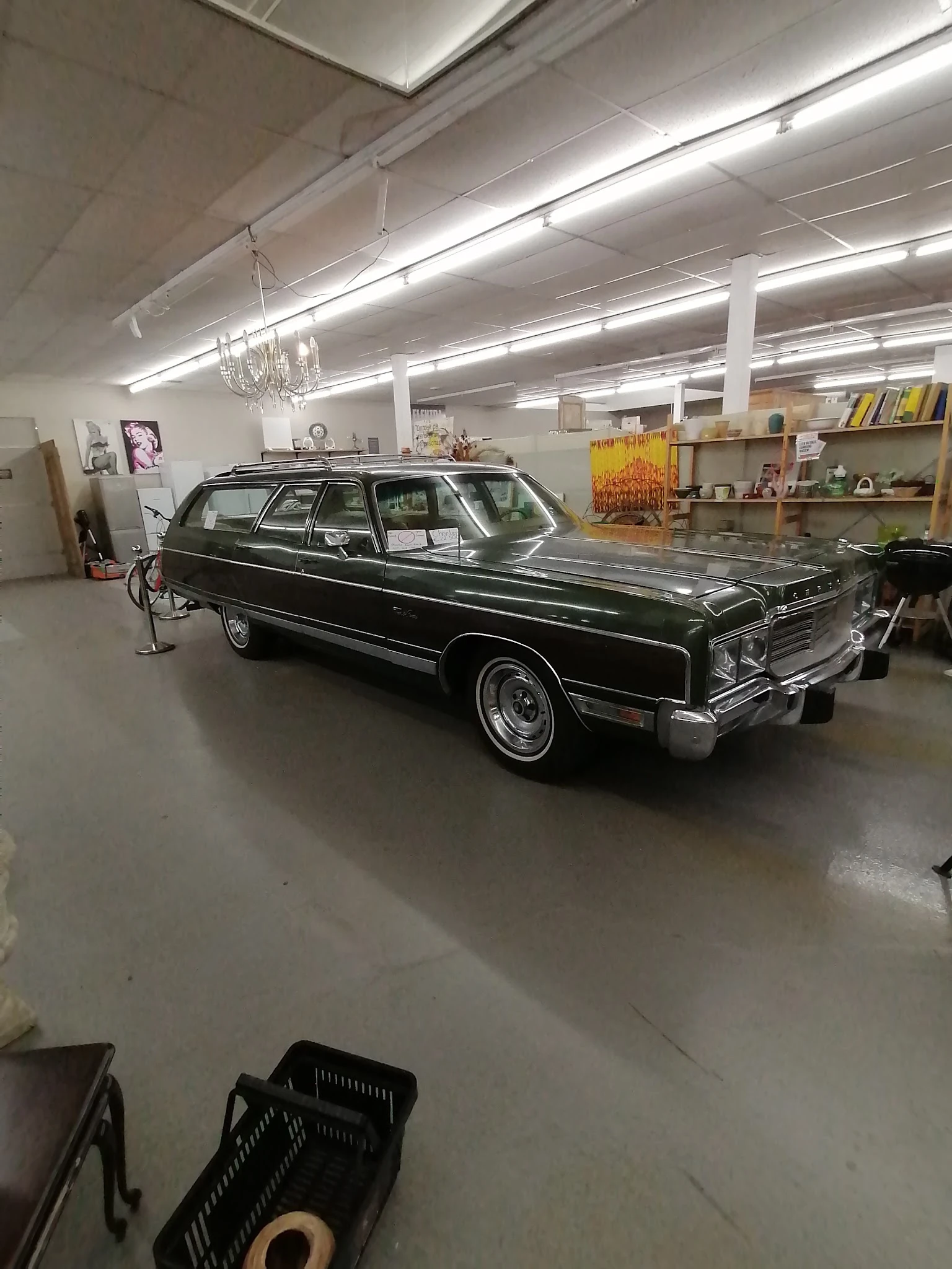 Zwarte klassieke Amerikaanse auto in een helder verlichte winkelruimte met stellingen en artikelen op de achtergrond