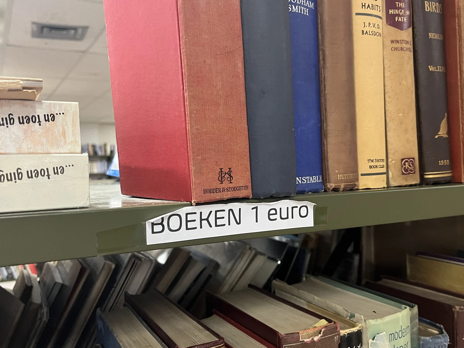 Boekenrek met oude en antieke boeken, waarvan enkele met gekleurde ruggen, met prijskaartje 'BOEKEN 1 euro'