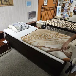 Tweedehands bedframe met witte matras en getoonde dekens in showroom
