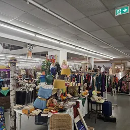 Overzicht van de winkelvloer met kledingrekken, meubels en spullen uitgestald in een grote ruimte met grijs plafond