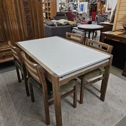 Rechthoekige houten eettafel met witte blad en bijbehorende stoelen in kringloopwinkel.