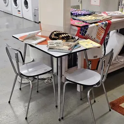 Eettafel met twee stoelen en stapels spullen op de tafel en op een rood rek op de achtergrond