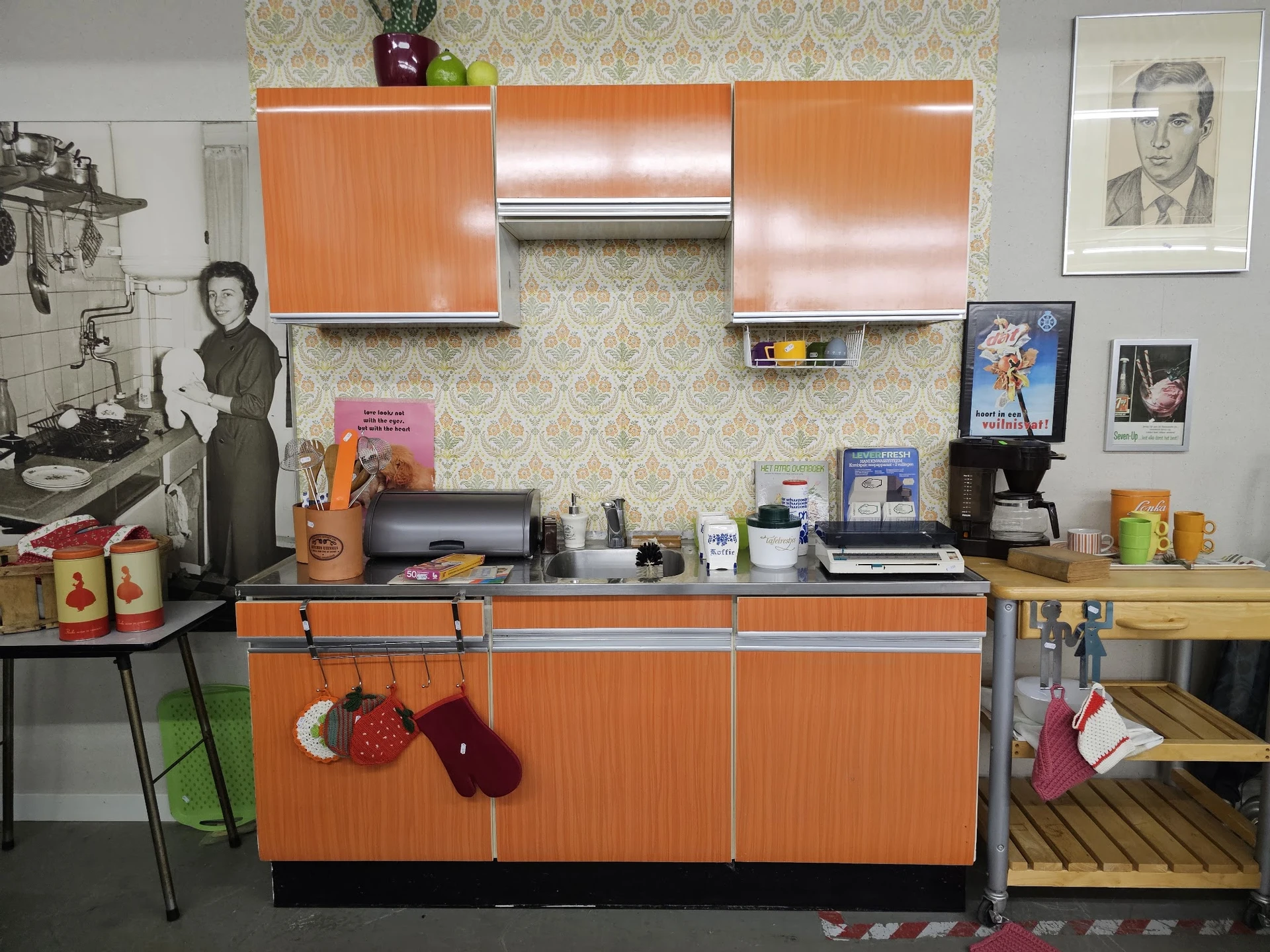 Vintage keukenhoek met oranje kasten, retro accessoires en muurdecoratie in kringloopwinkel
