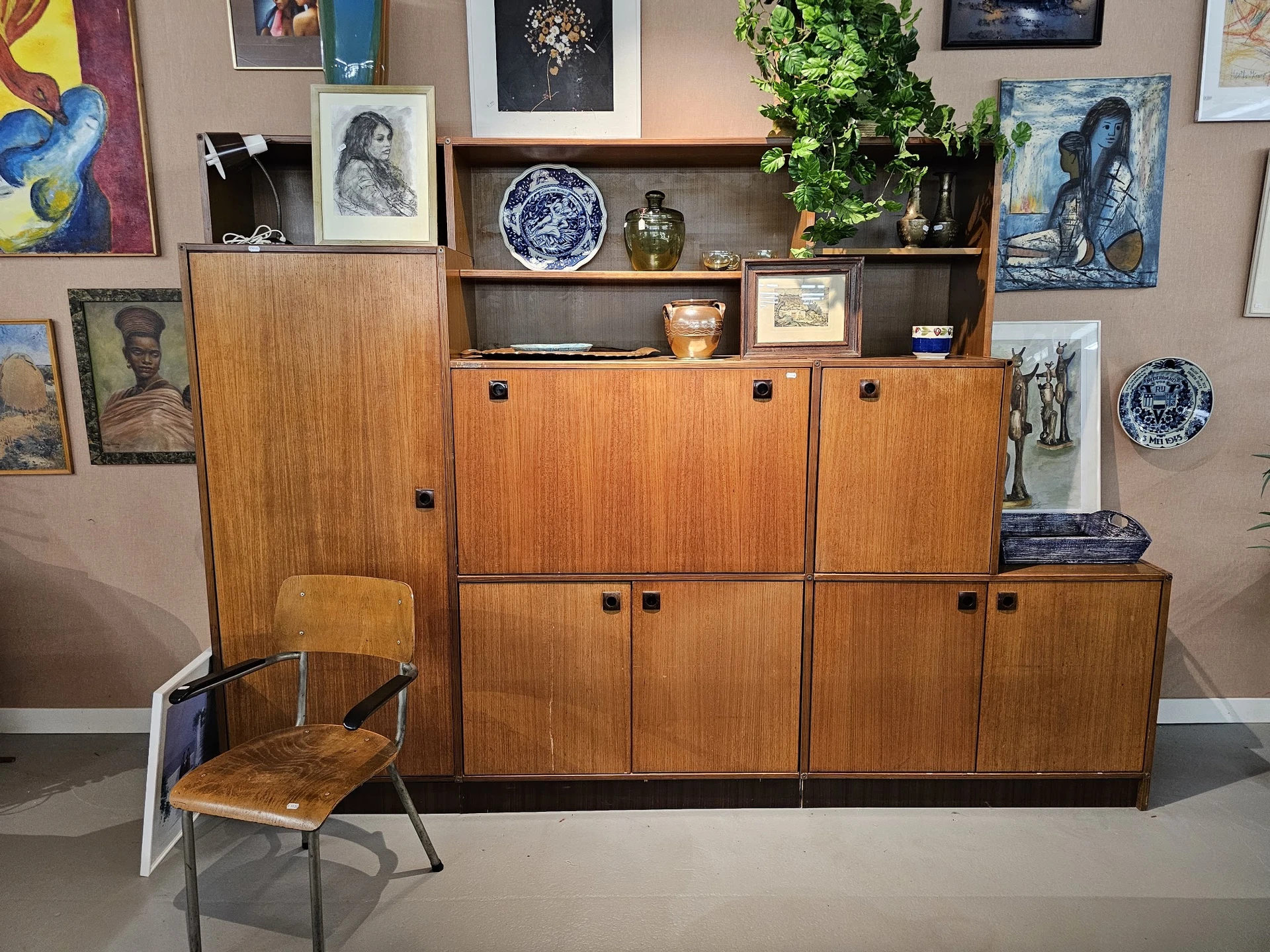 Houten vintage dressoir met meerdere kastdeuren en open schappen, voorzien van decoratieve objecten, schalen en planten.