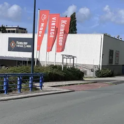 Voorgevel van kringloopwinkel met rode banners, witte golfplaten en ingang met trap