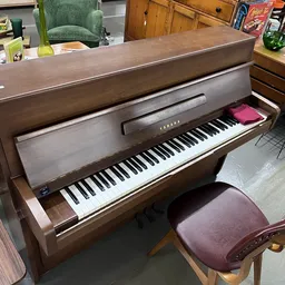 Bruine houten piano met toetsen en paarse pianokruk in een kringloopwinkel
