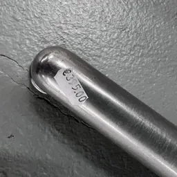 Close-up van een zilveren metalen voorwerp met gravering tegen een grijze muur.