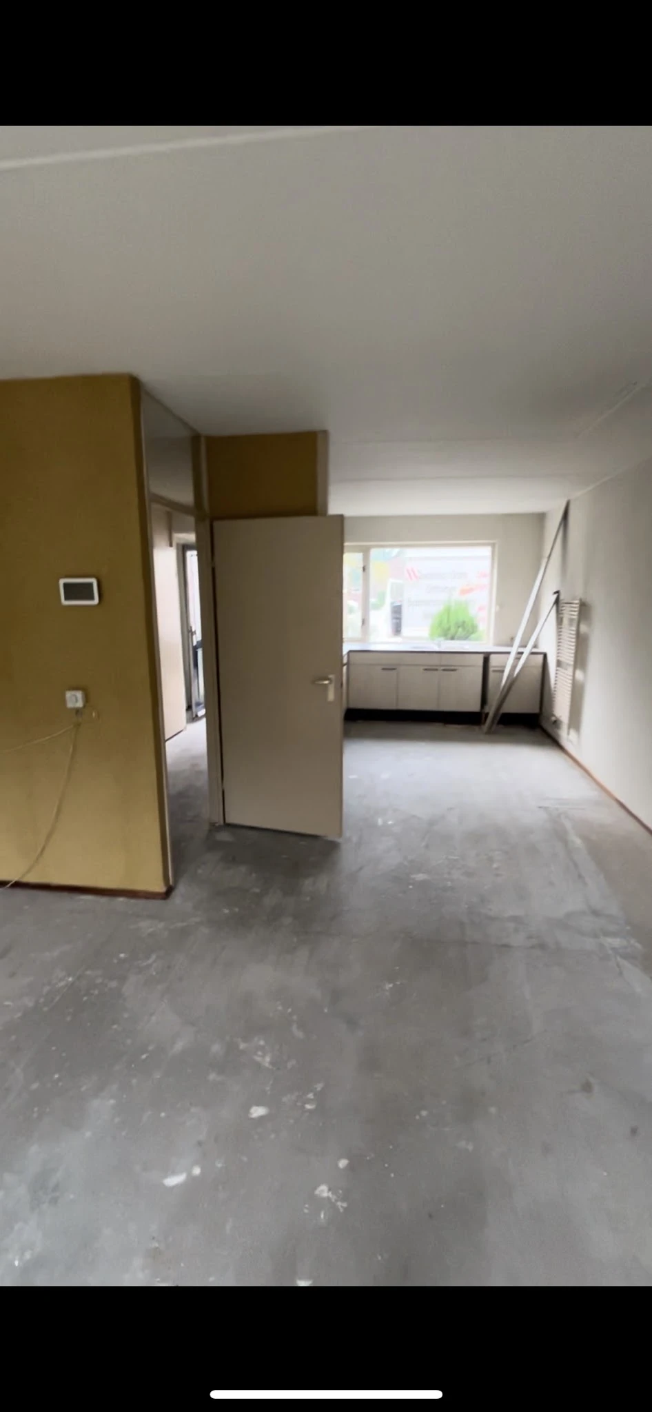 Lege winkelruimte met grijze vloer, witte wanden en een open deur, enkele stellingen zichtbaar