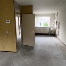 Lege winkelruimte met grijze vloer, witte wanden en een open deur, enkele stellingen zichtbaar