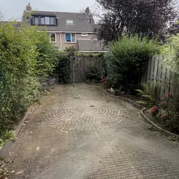 Achtertuin met grindpad en houten schutting omgeven door struiken
