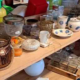 Tafel met diverse huishoudelijke artikelen: glazen potten, aardewerk servies met blauwe decoratie, woven manden, kandelaars e