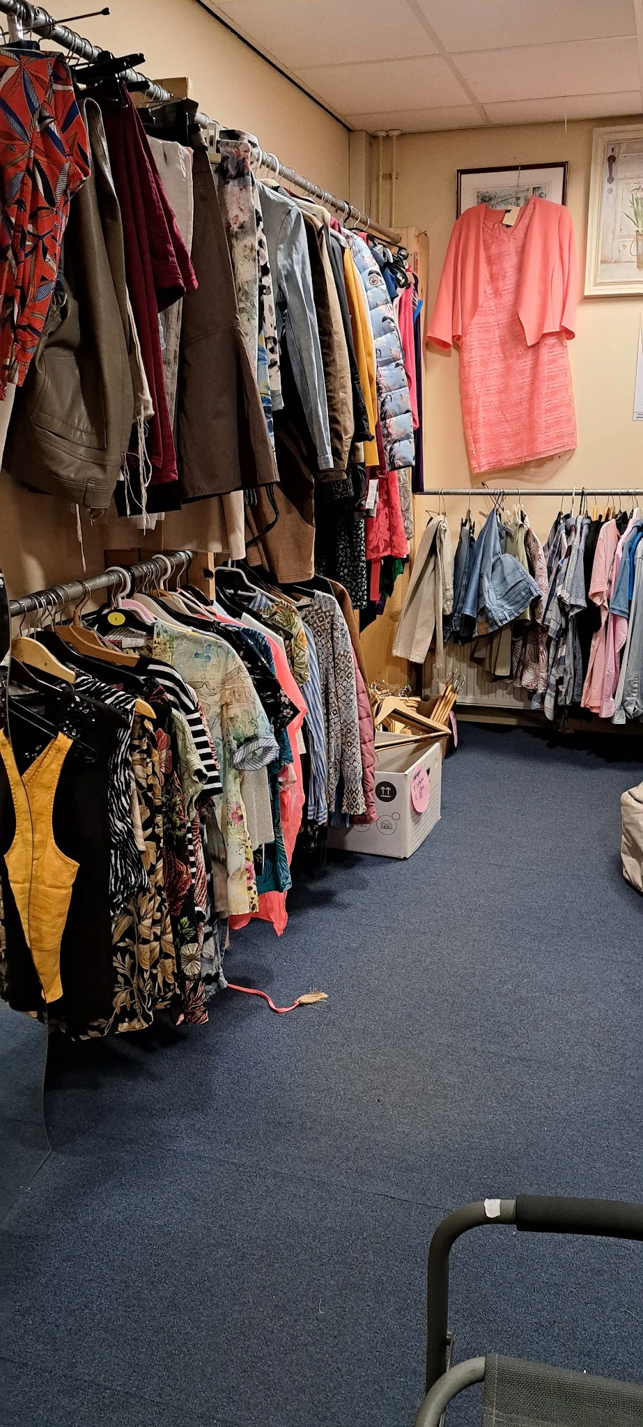 Rekken met tweedehands kleding op hangers, waaronder jassen, jurken en shirts in verschillende kleuren en patronen