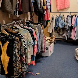Rekken met tweedehands kleding op hangers, waaronder jassen, jurken en shirts in verschillende kleuren en patronen