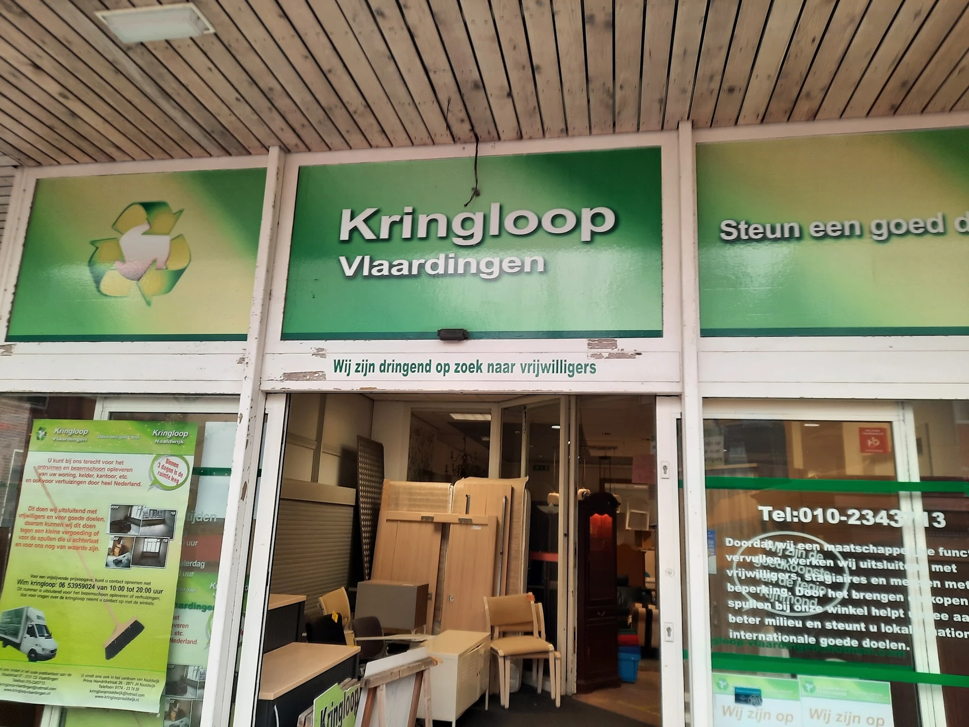 Winkelpui van Kringloop Vlaardingen met groene borden en ingang, stellingen met dozen en spullen zichtbaar