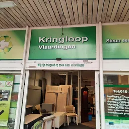 Winkelpui van Kringloop Vlaardingen met groene borden en ingang, stellingen met dozen en spullen zichtbaar