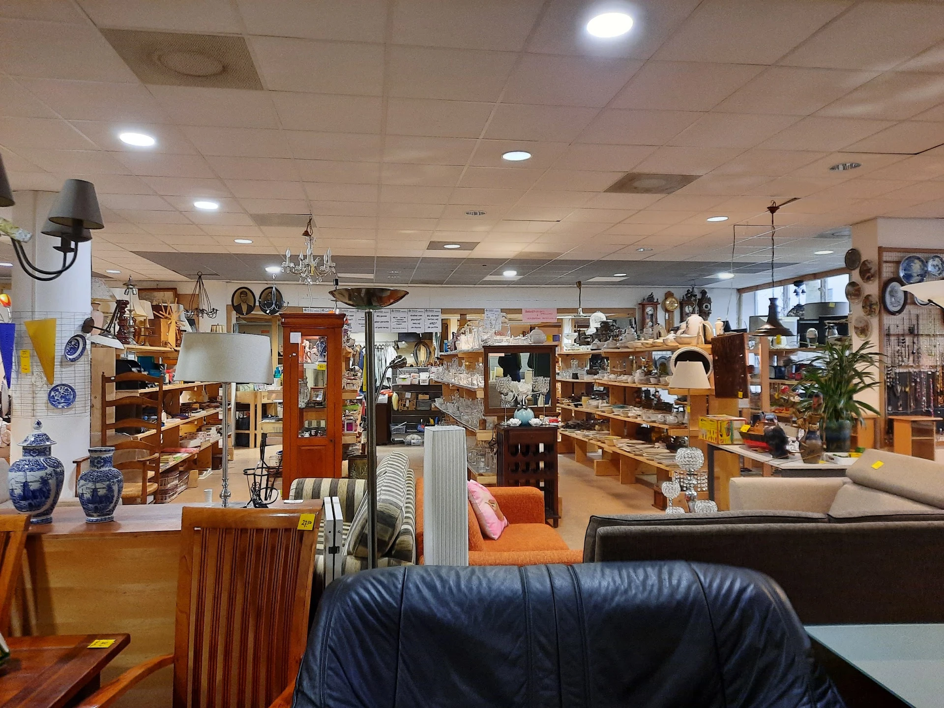 Winkelvloer van kringloopwinkel met verschillende rekken, stellingen en uitgestalde huishoudartikelen, meubels en decoratieve