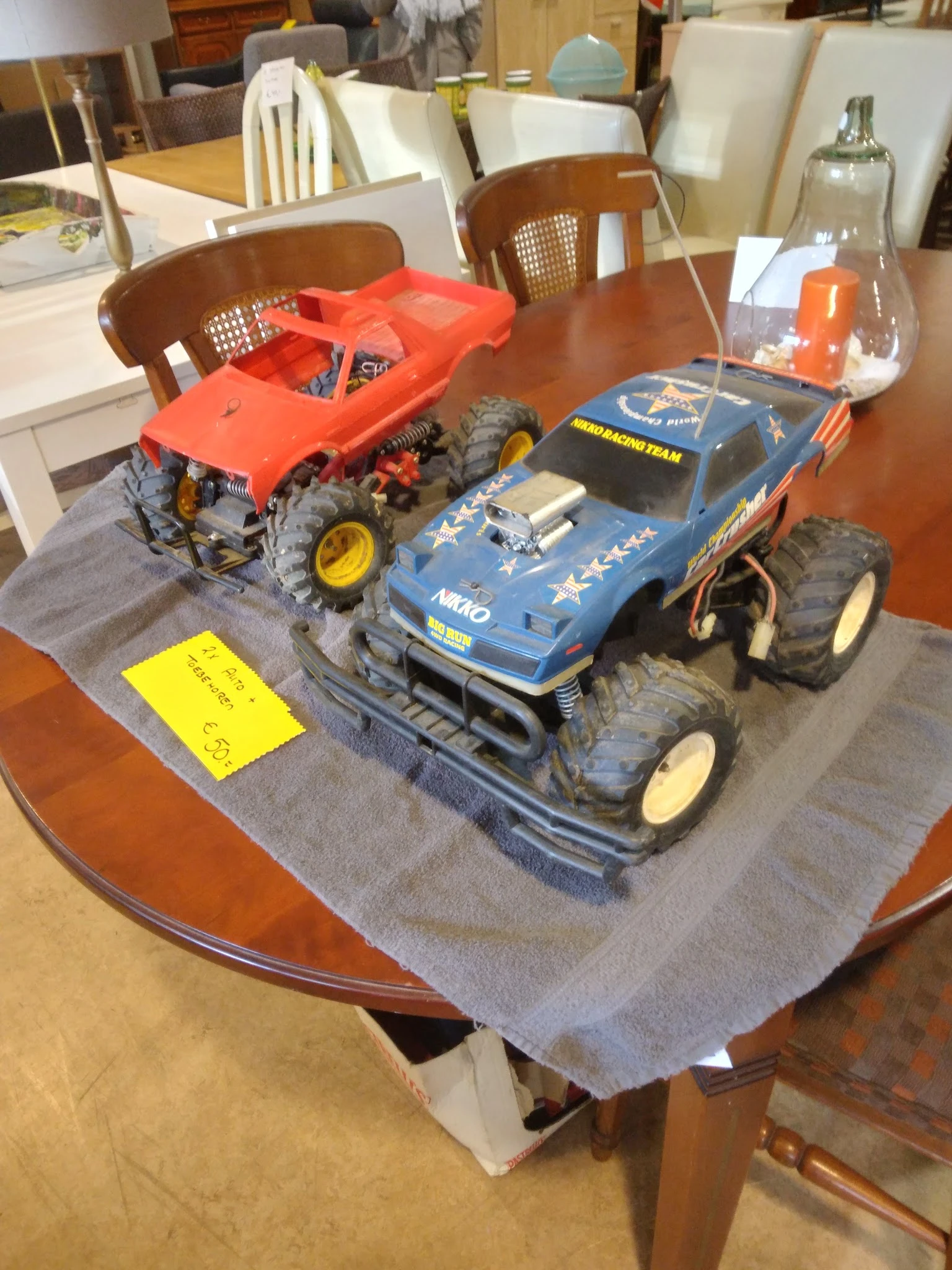 Twee speelgoedauto's op een grijze doek op een tafel, waaronder een geel kaartje