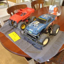 Twee speelgoedauto's op een grijze doek op een tafel, waaronder een geel kaartje