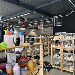 Overzicht van kringloopwinkel met houten stellingen vol huishoudartikelen, servies en keukenspullen