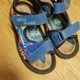 Blauwe kindersandalen met surfmotief en tekst 'surfing the waves', close-up op houten ondergrond