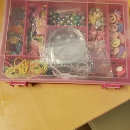 Roze opbergdoos met kralen, parels en sieraden, met een doorzichtige plastic armband op het deksel