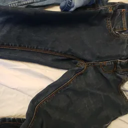 Donkerblauwe jeans met slijtage, uitgestald op wit materiaal