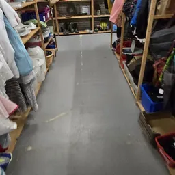 Binnenaanzicht van een kringloopwinkel met houten stellingen vol met kleding en dozen langs de zijkanten
