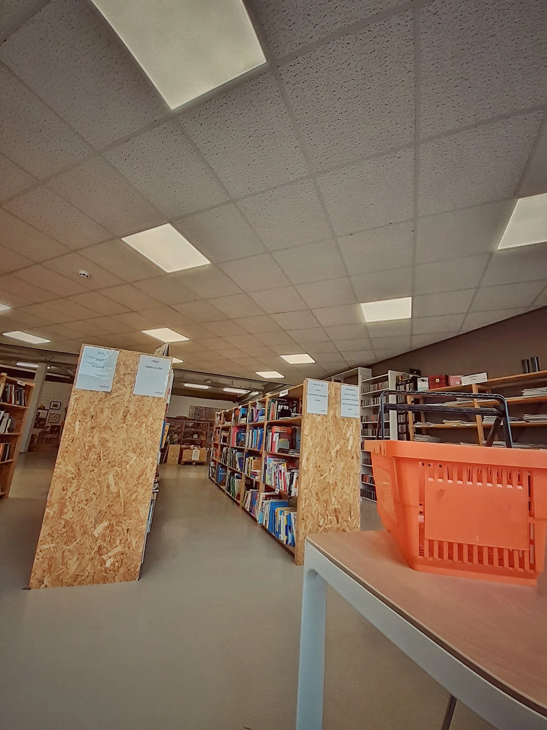 Boeken in kasten en op stellingen in een kringloopwinkel, met oranje plastic kratten op de vloer