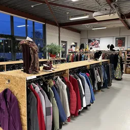 Winkelvloer met kledingrekken vol tweedehands kleding, houten toonbank en grote ramen met avondlicht