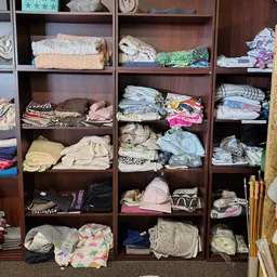 Houten stellingen gevuld met opgevouwen kleding in verschillende kleuren en materialen