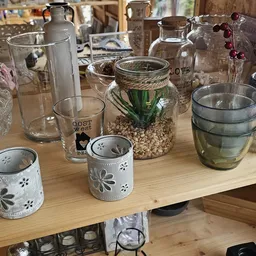Tafel met diverse glazen vazen, potjes en decoratieve items zoals glazen met patronen en een pot met stenen en groene plant