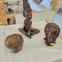 Drie houten beelden en sculpturen: een hoofd met golvend haar, een zittend figuur en een busteportret