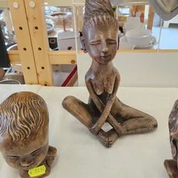 Houten beeldhouwwerk van zittend figuur met gekruiste benen op display
