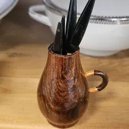 Houten kan met zwarte handvaten gevuld met keukengereedschap op houten werkblad